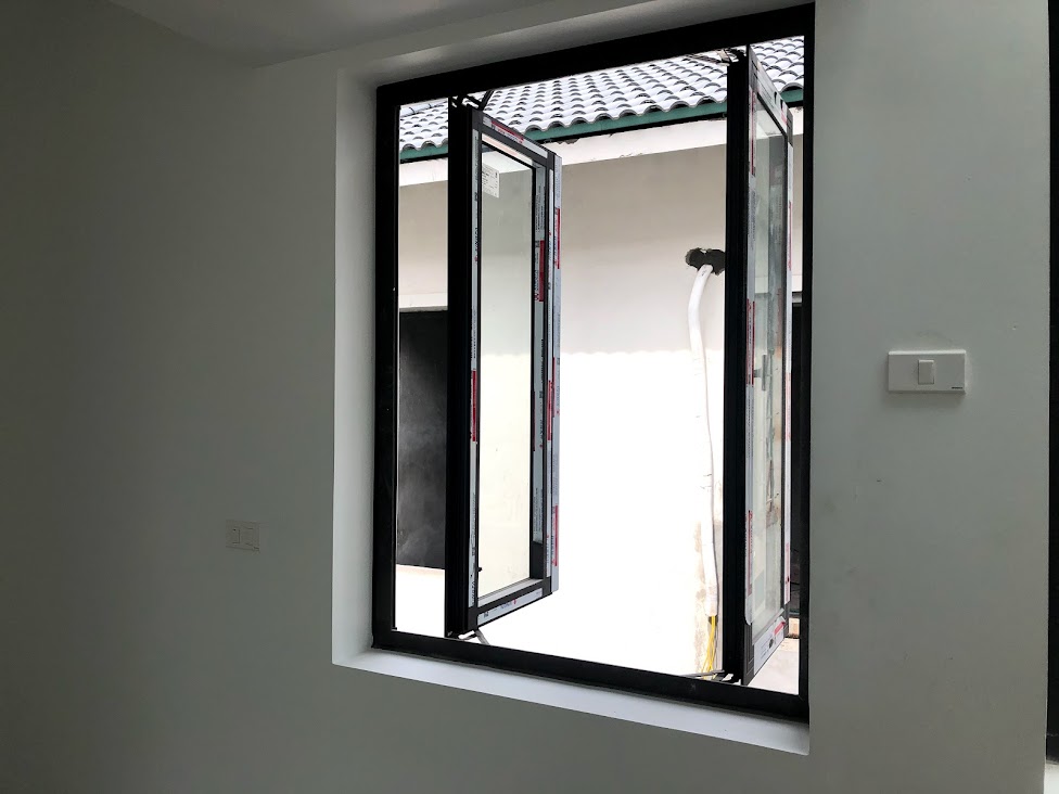 Cửa sổ nhôm kính mở quay màu đen trong phòng, nhìn ra mái ngói xanh bên ngoài